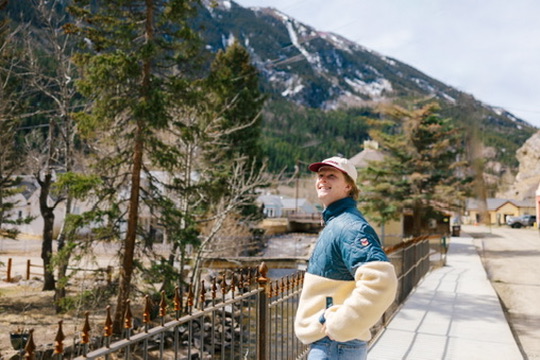 Kaiden standing beside a mountain village in a blue and cream jacket